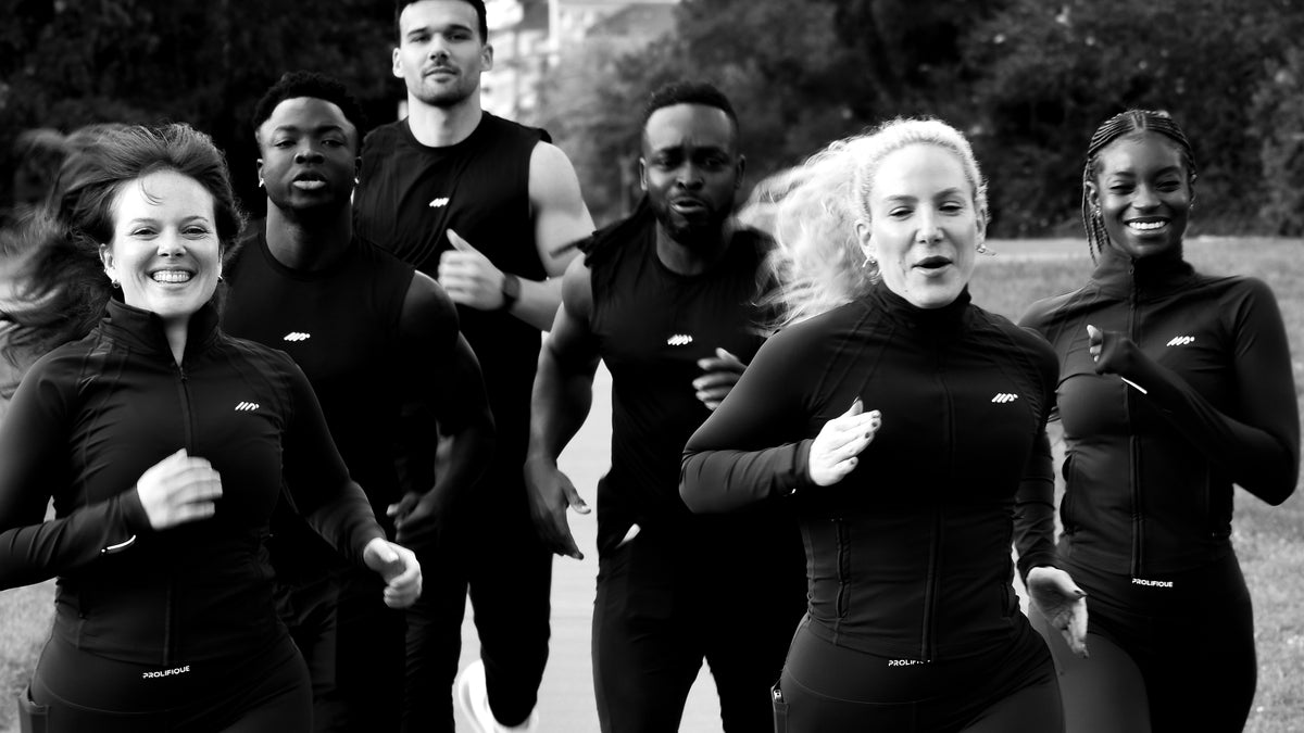 A group of people jogging outdoors with the central focus on a woman wearing Prolifique maroon long-sleeve jacket and matching leggings. Other runners in Prolifique black air-flow singlet and pants are visible behind her shown in a black-and-white photograph. 